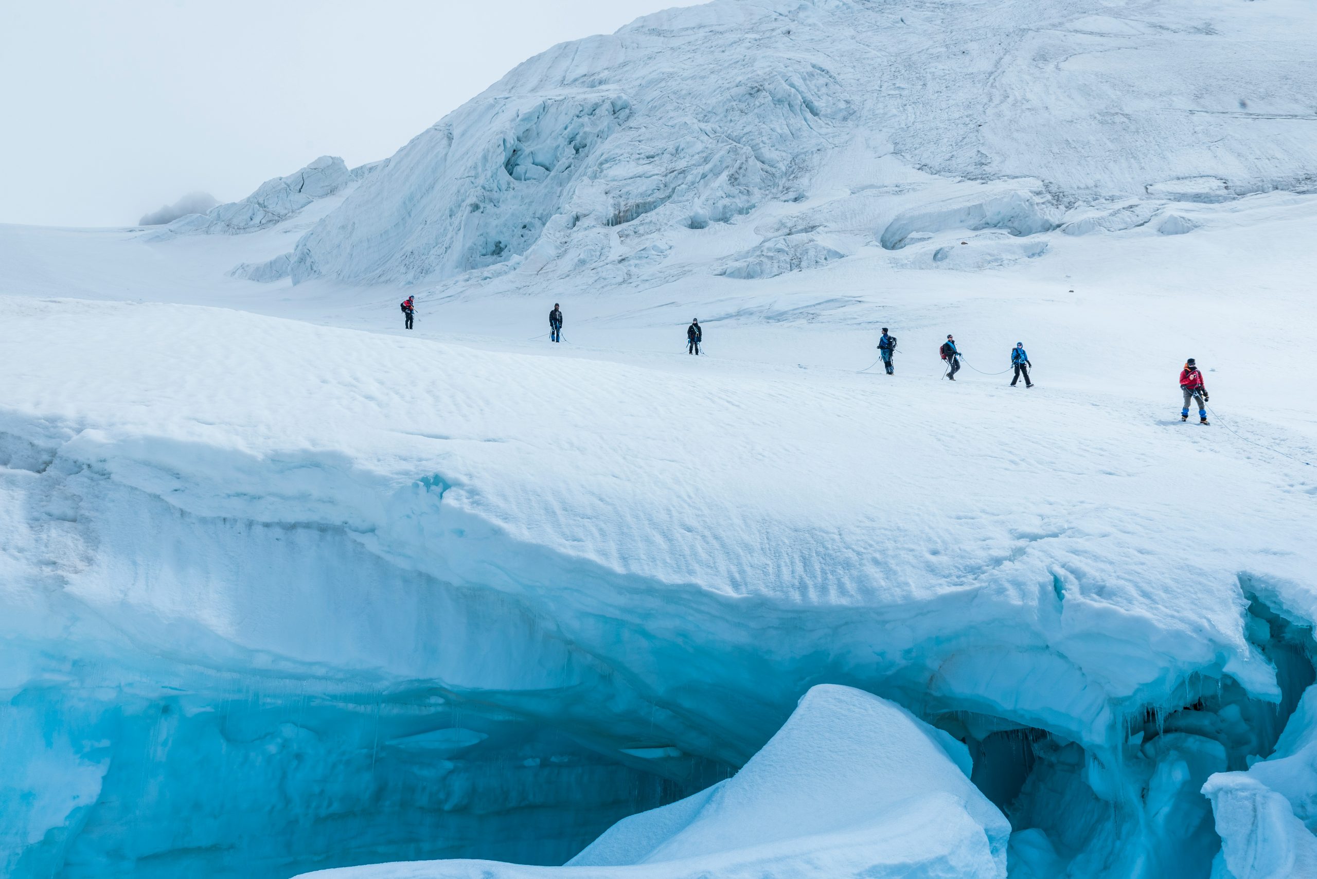 Guided group roped up crossing a glacier, with crevasses visible